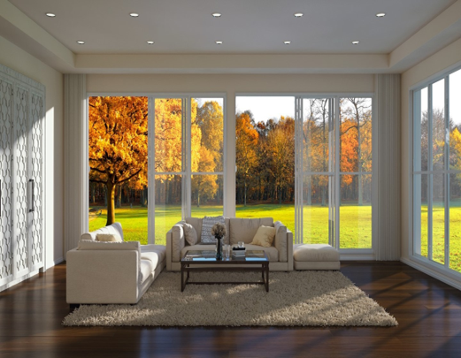 The interior of a sunroom with wood flooring with an area rug over it, two couches and a coffee table, recessed ceiling lights, and two open sliding glass doors with trees with fall foliage outside.